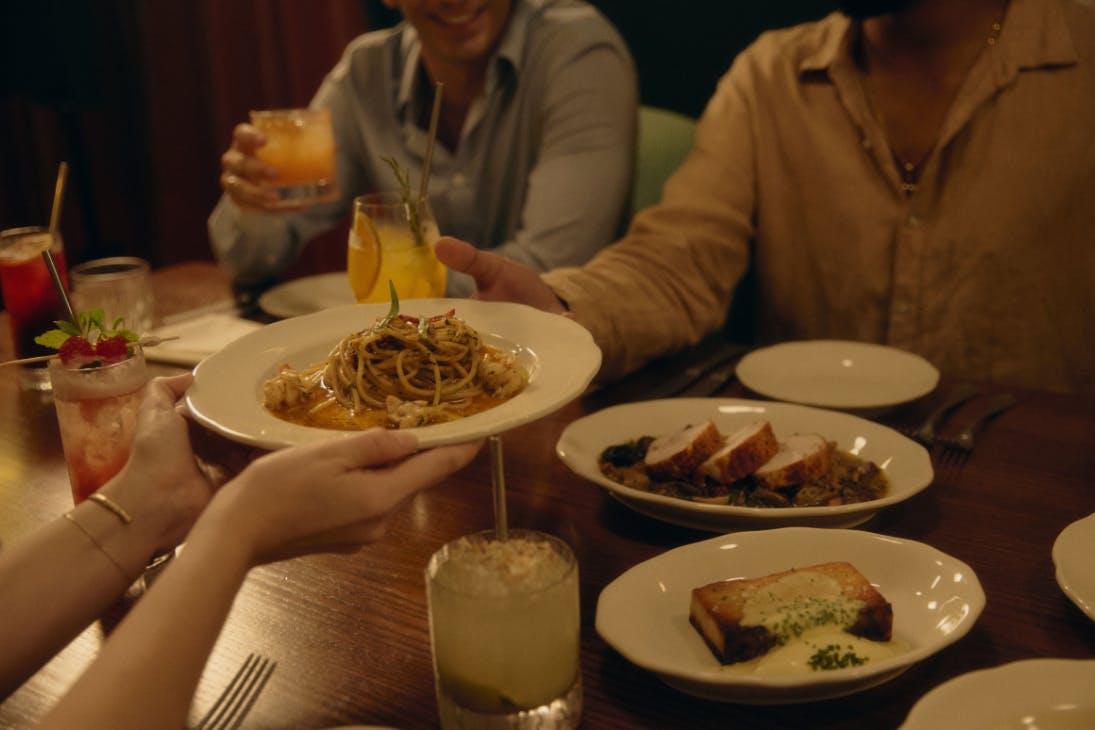 Plate of pasta being passed across table of Italian food and drinks